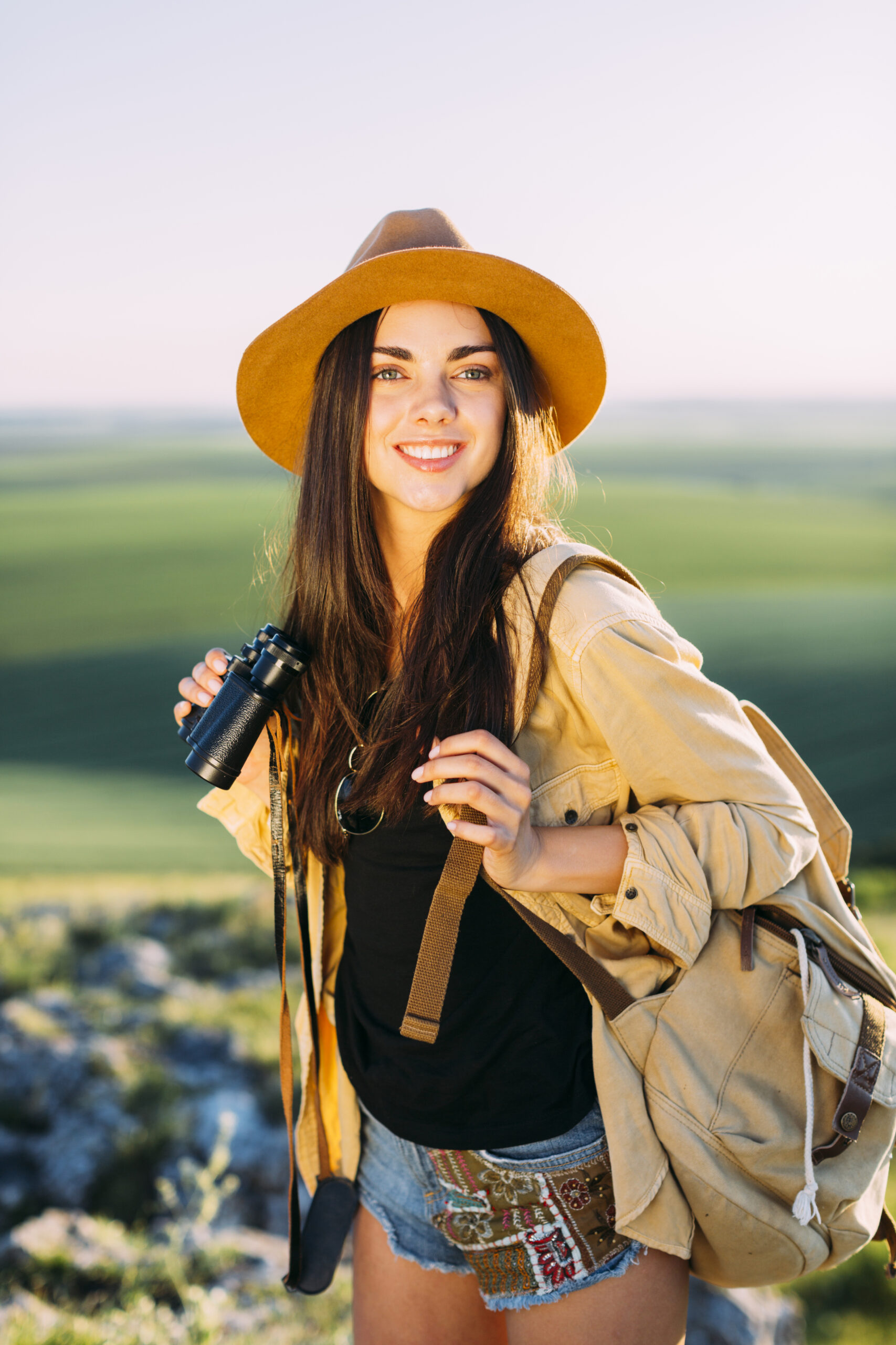 happy young solo traveler with backpack and binoculars